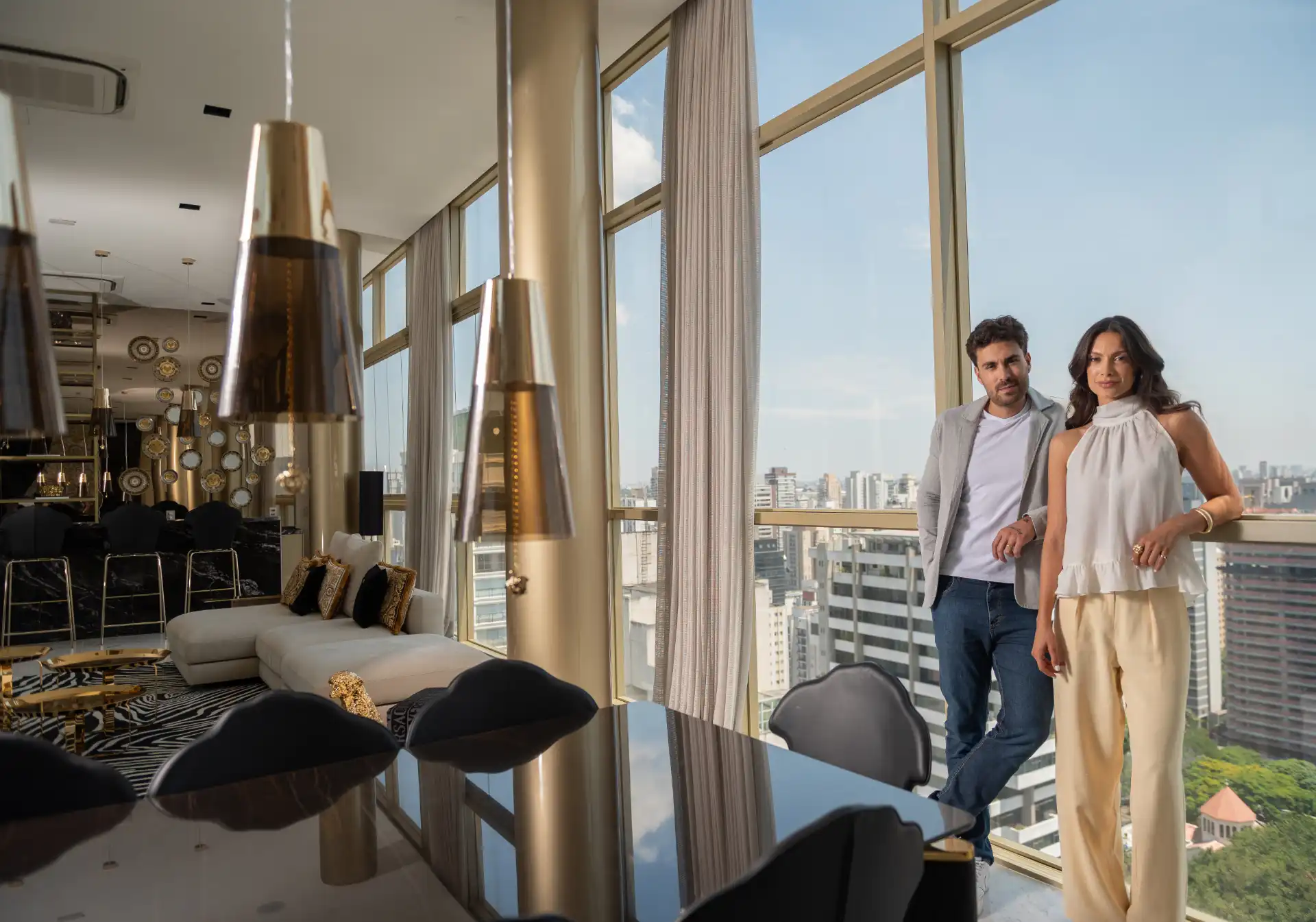 Imagem de um apartamento de alto padrão com vista panorâmica da cidade, sala moderna com decoração elegante, com um casal posando na varanda.