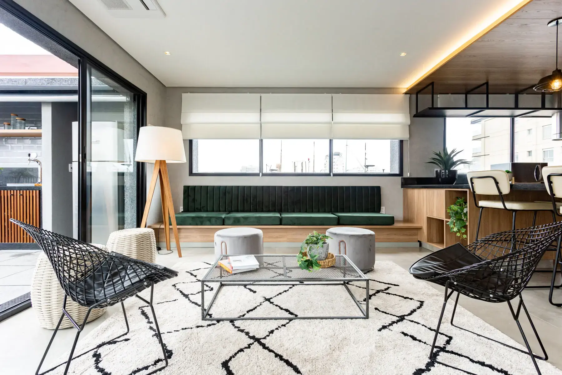 Sala de estar moderna e elegante com sofá verde, poltronas de vime, mesa de centro de vidro, luminária de pé, janelas grandes, decorada com plantas e iluminação aconchegante, ideal para ambientes residenciais contemporâneos.