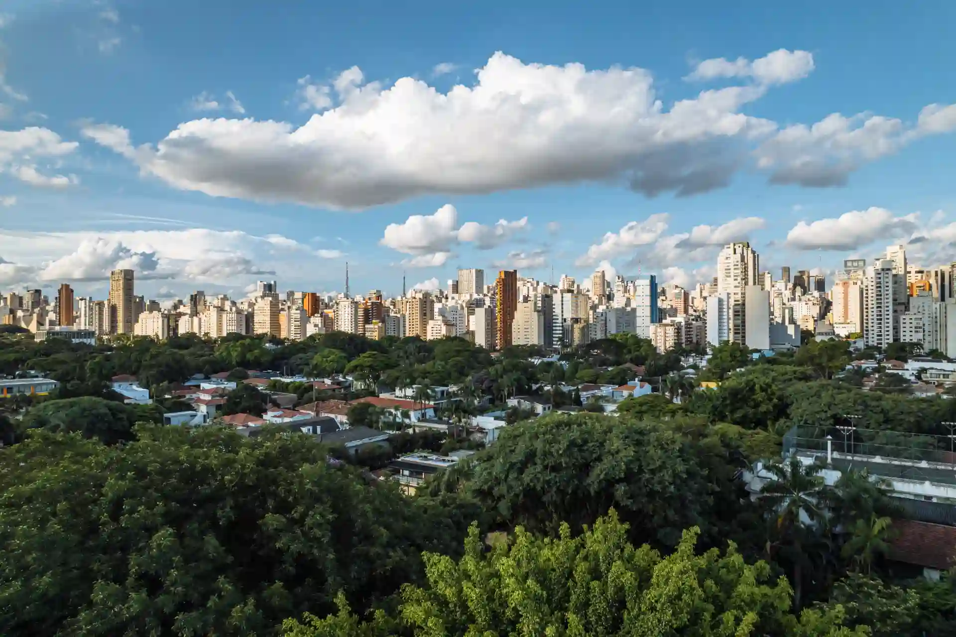 Vista panorâmica de uma cidade moderna com arranha-céus e muito verde, sob céu com nuvens brancas. Ideal para quem busca imagens de cidades grandes e arquitetura urbana.
