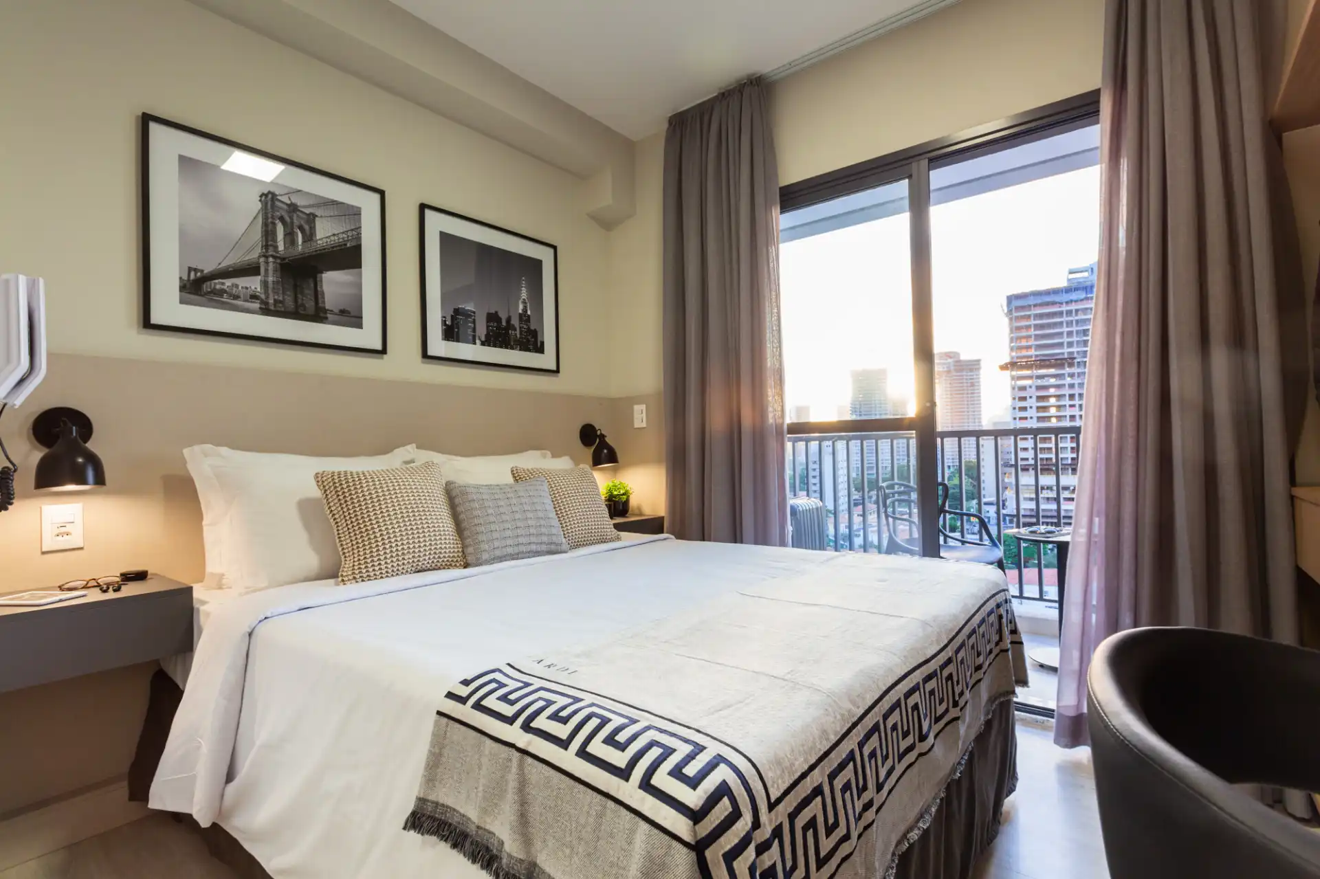 Quarto de hotel moderno com cama confortável, decoração elegante, janelas grande com vista para a cidade e iluminação natural, ideal para hospedagem confortável.