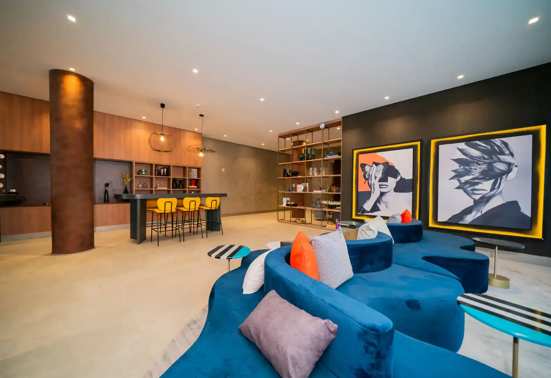 Sala moderna e aconchegante com sofá azul, decoração contemporânea, quadros artísticos na parede, biblioteca com prateleiras, iluminação embutida e decoração elegante.